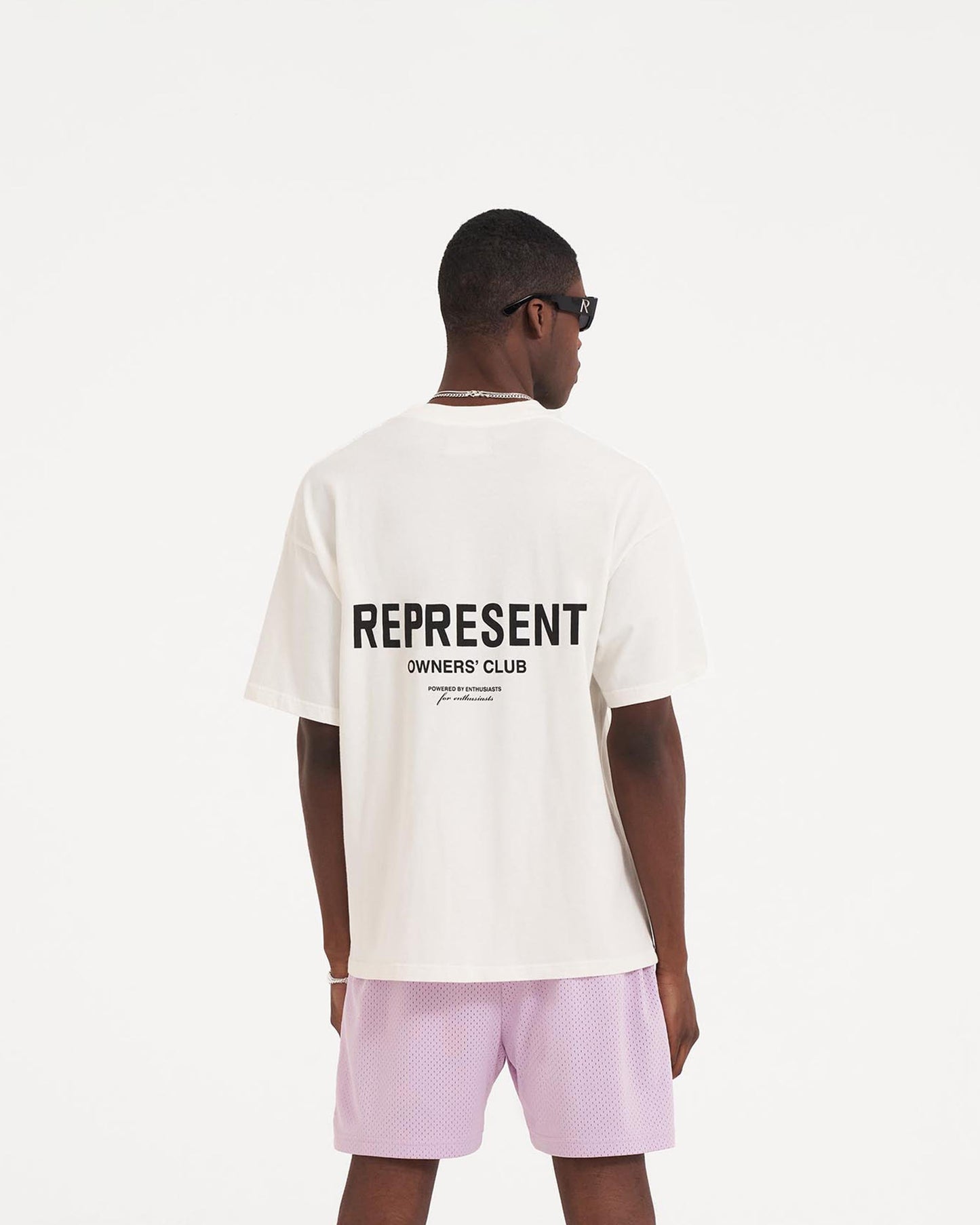 Man wearing an oversized white t-shirt on a plain white background | Represent Owners Club T-Shirt in Flat White | Short sleeve jersey t-shirt with graphic branding | Owners Club T-Shirts | Represent Clo
