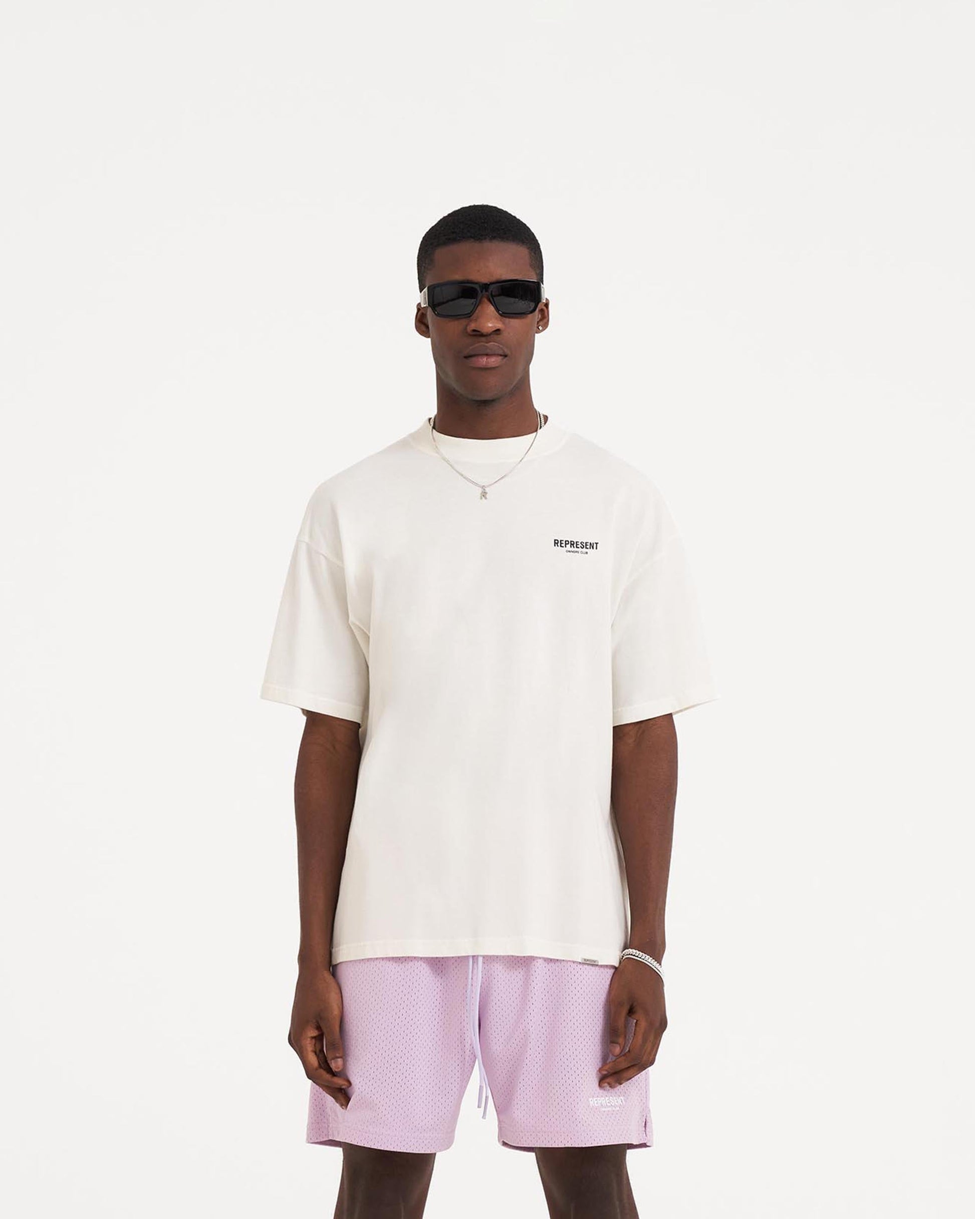 Man wearing an oversized white t-shirt on a plain white background | Represent Owners Club T-Shirt in Flat White | Oversized jersey t-shirt with graphic branding | Owners Club T-Shirts | Represent Clo