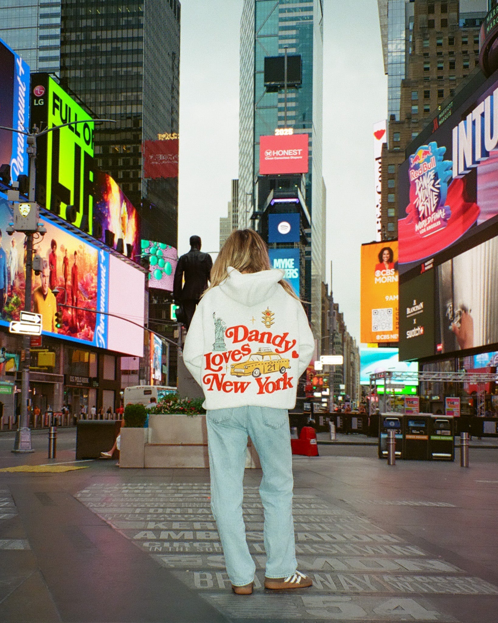 Person wearing a sweatshirt with 'Dandy Loves New York' text in Times Square, New York.