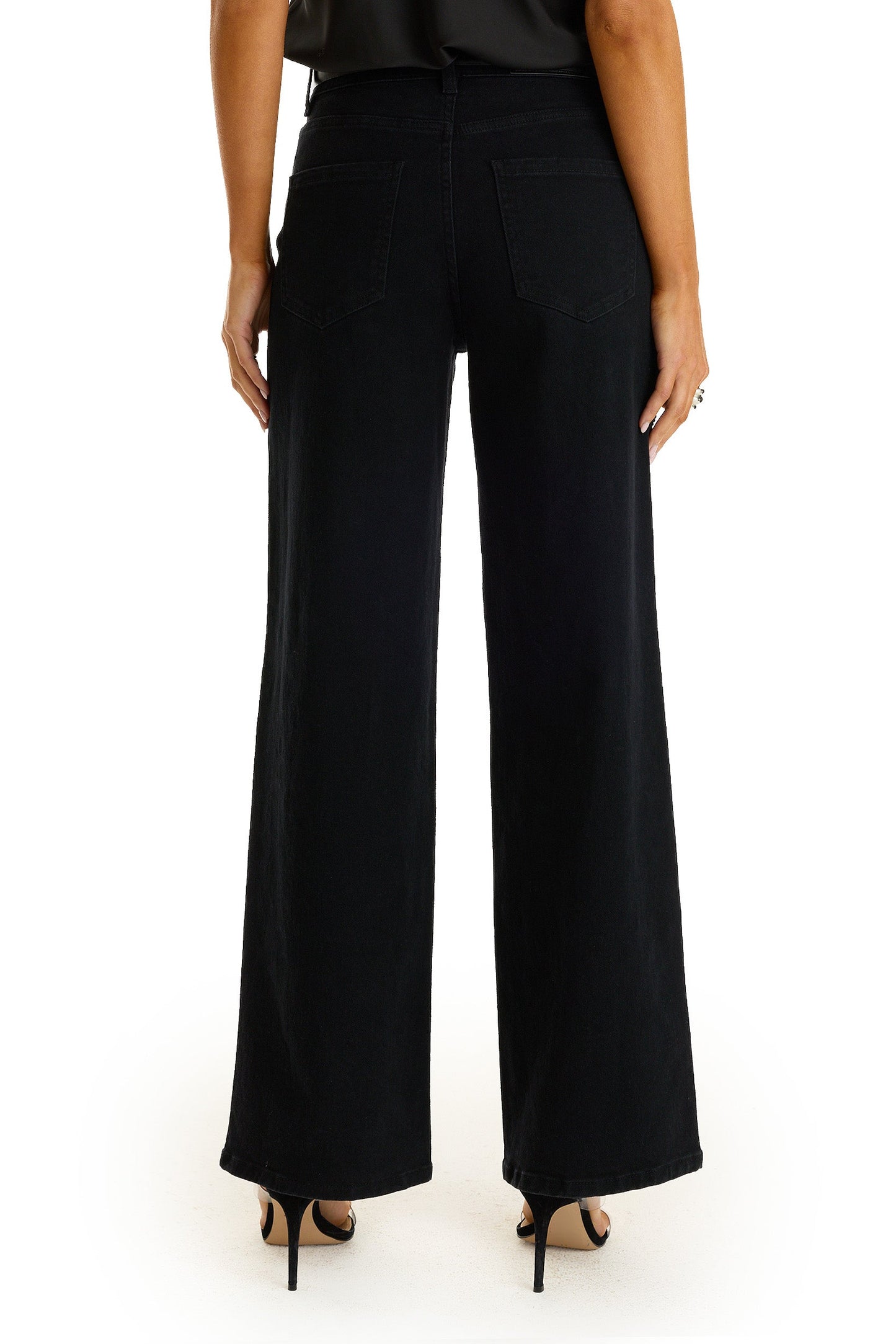 A person is shown from the back, standing against a white background, wearing the Kaia Pearl High Rise Jean in black and black high-heeled sandals.