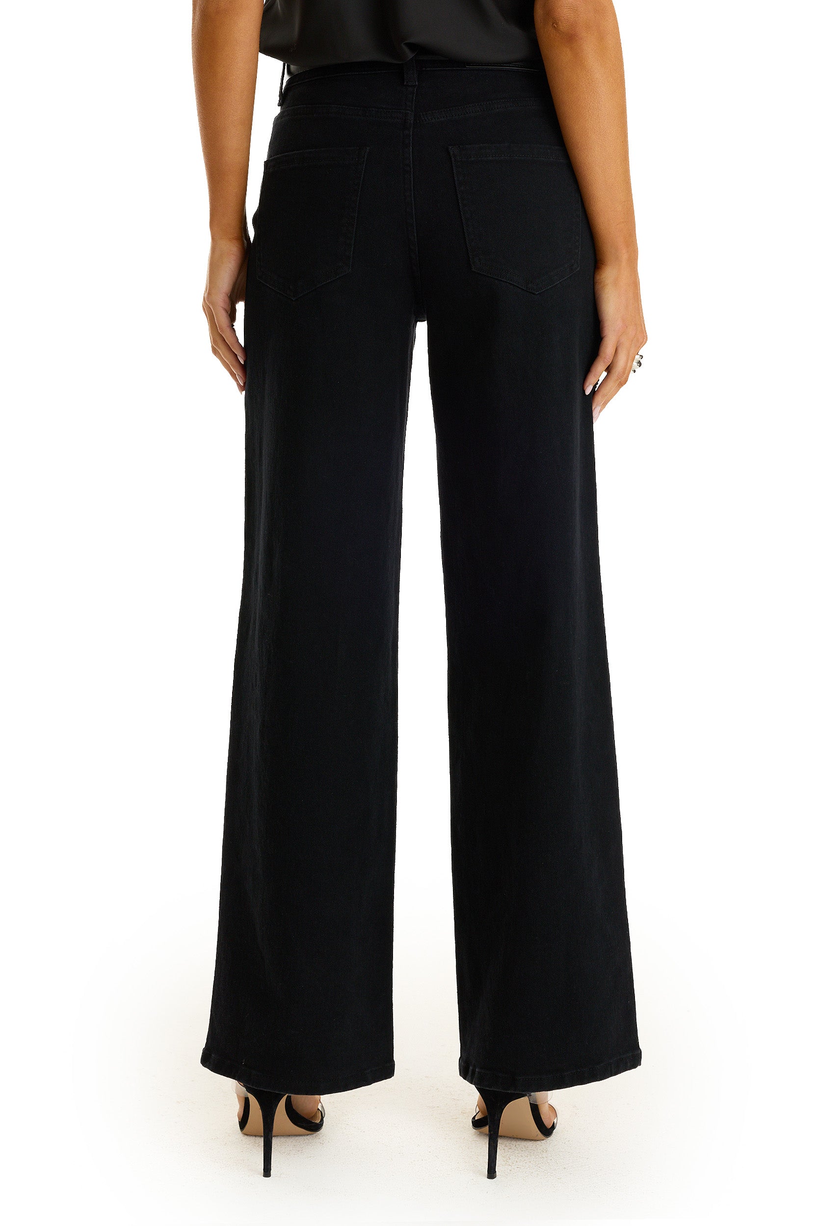 A person is shown from the back, standing against a white background, wearing the Kaia Pearl High Rise Jean in black and black high-heeled sandals.