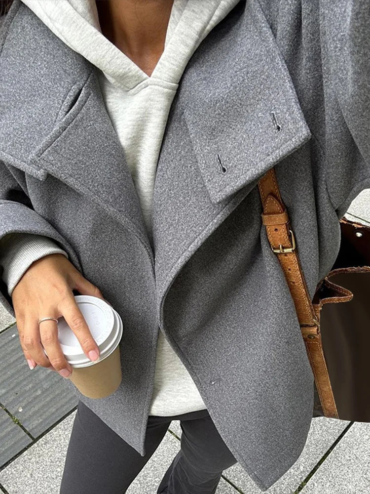 Black high-neck jacket with asymmetrical buttons and structured silhouette, featuring wide sleeves and a minimalist design for modern everyday styling.