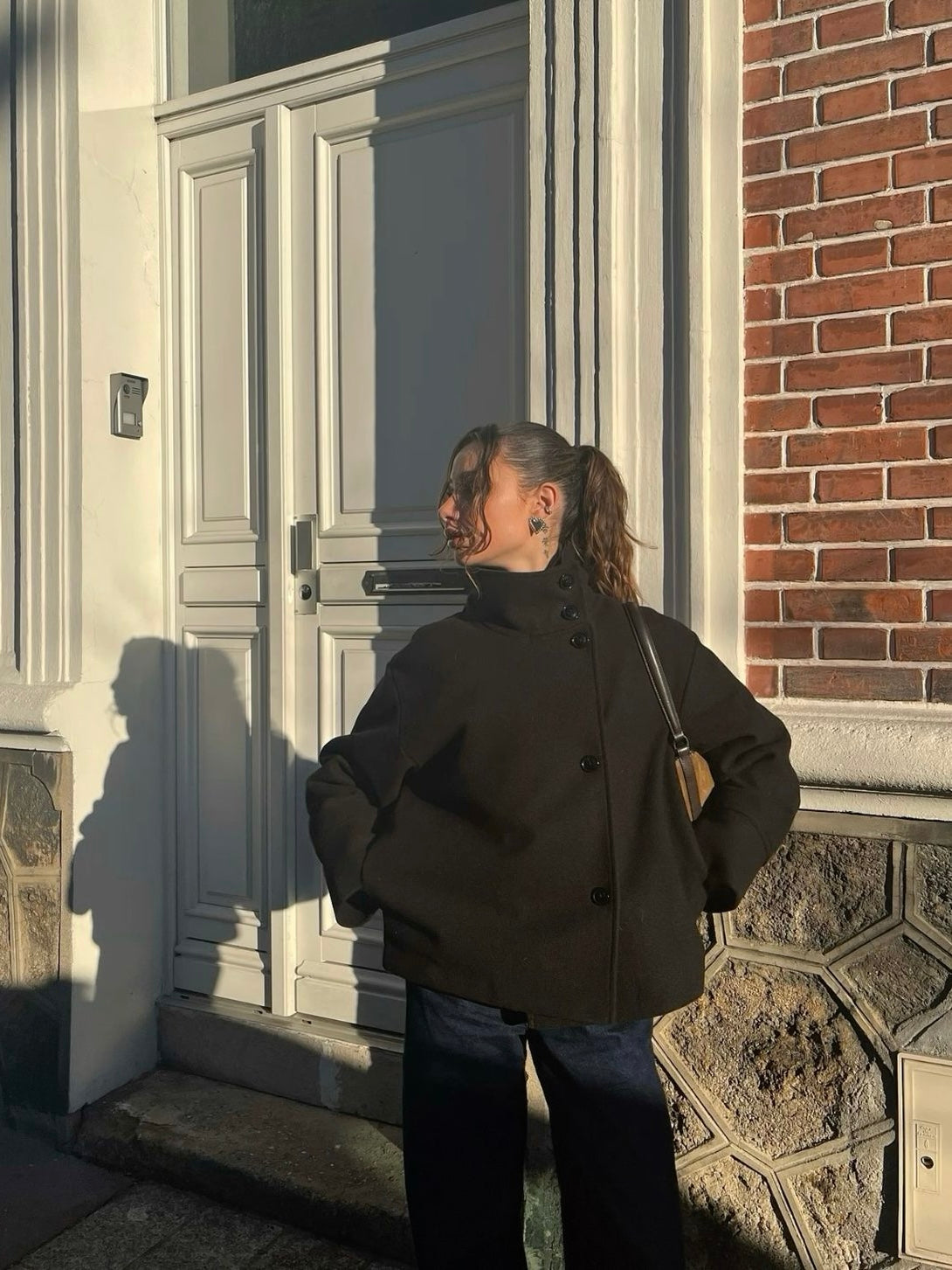 Black high-neck jacket with asymmetrical buttons and structured silhouette, featuring wide sleeves and a minimalist design for modern everyday styling.