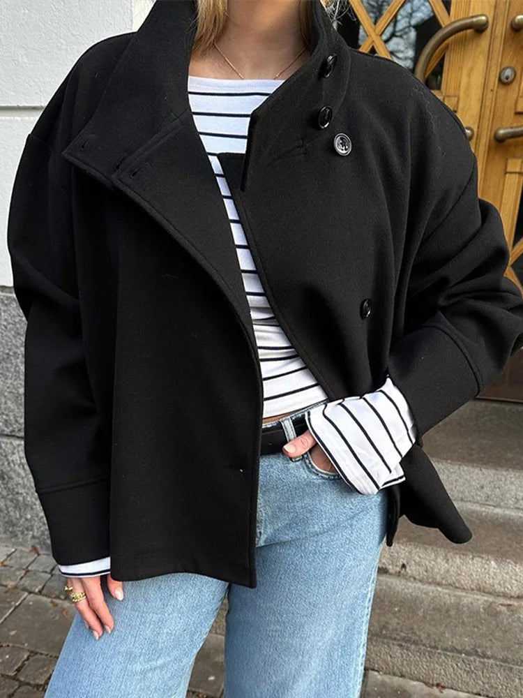 Black high-neck jacket with asymmetrical buttons and structured silhouette, featuring wide sleeves and a minimalist design for modern everyday styling.